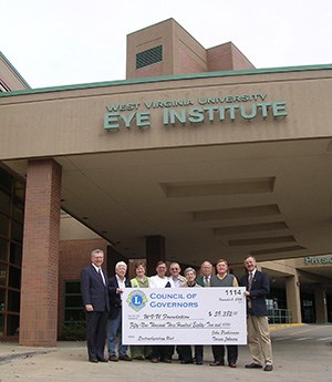 Lions group outside the eye institute building holding a giant check in a group formation.