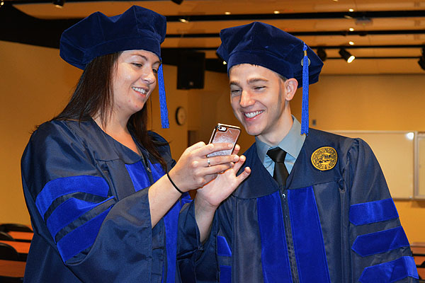 Amanda Suchanek and Daniel Murphy in graduation caps and gowns looking at a smart phone.