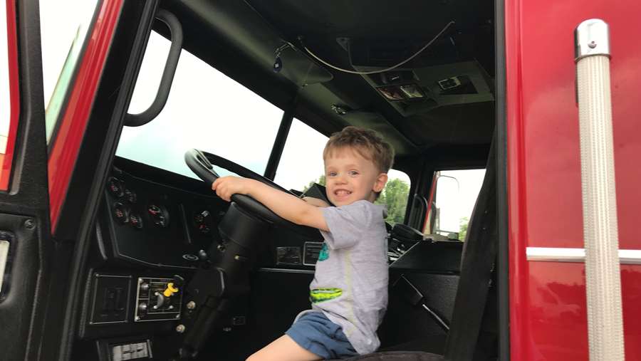 A Little Boy is seated in the Fire Truck and holding onto the steering wheel.