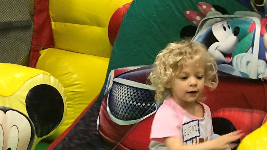 A little girl is reaching for the sides of the bounce house and jumping up and down.