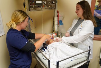 Students perform procedure on infant simulation manikin at neonatal training station