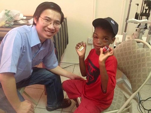 Dr. John Nguyen is kneeling next to a St.  Lucia child seated in a chair.
