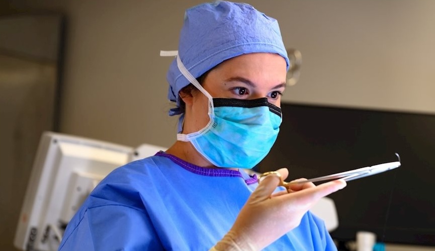 Dr. Andrea Pettit examines medical equipment while dressed in scrubs