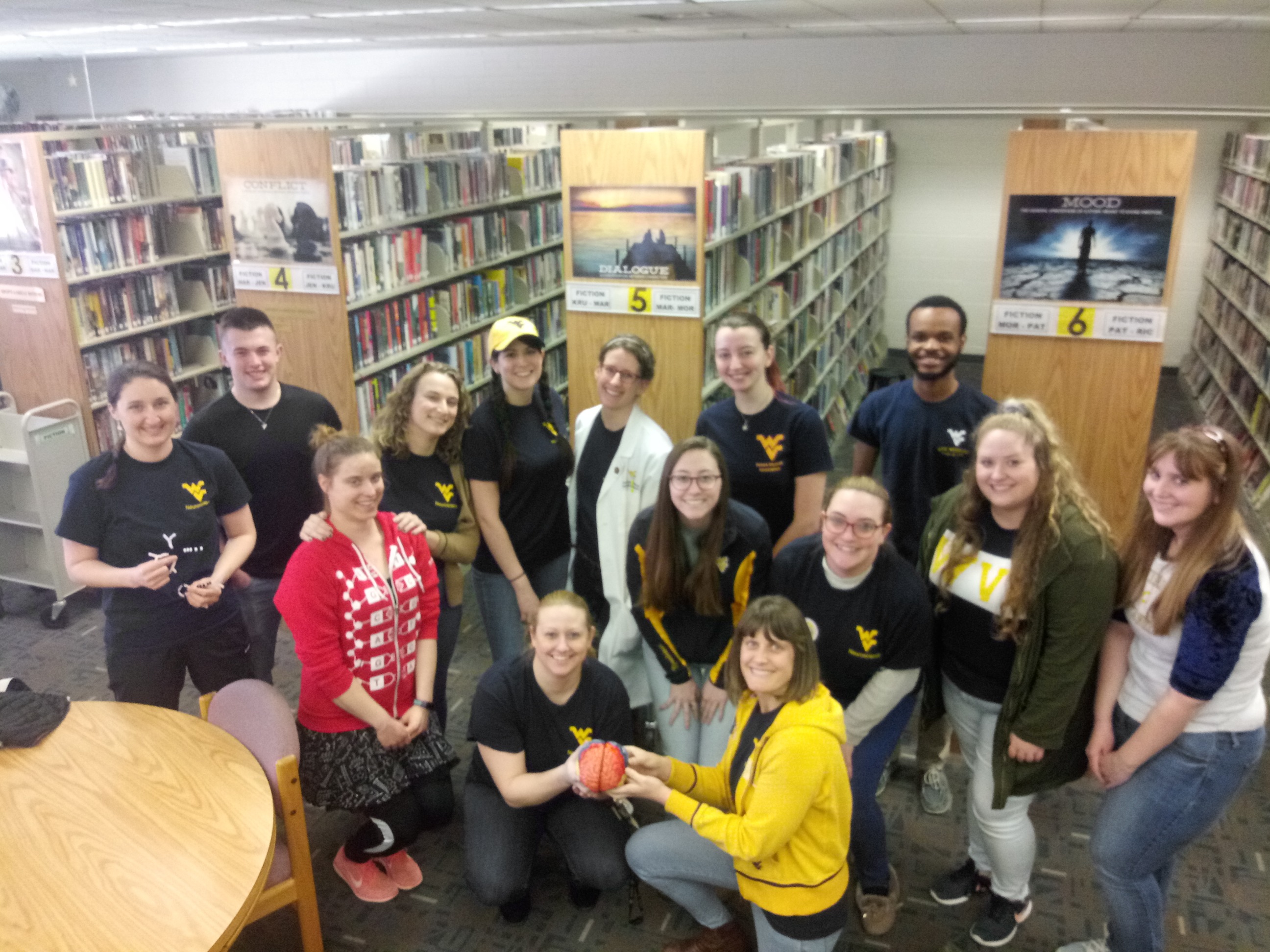 WVU Neuroscience Graduate Student Organization smiling in the library, holding a model of a brain
