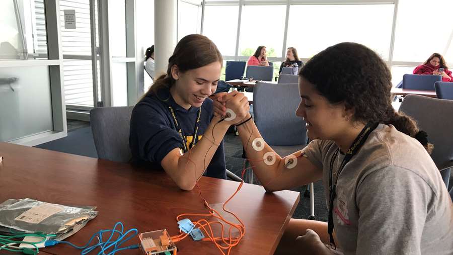 two female students arm wrestling with large muscle electrodes on arms